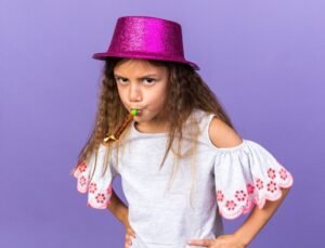 annoyed-little-caucasian-girl-with-violet-party-hat-blowing-party-whistle-isolated-purple-wall-with-copy-space_141793-97372